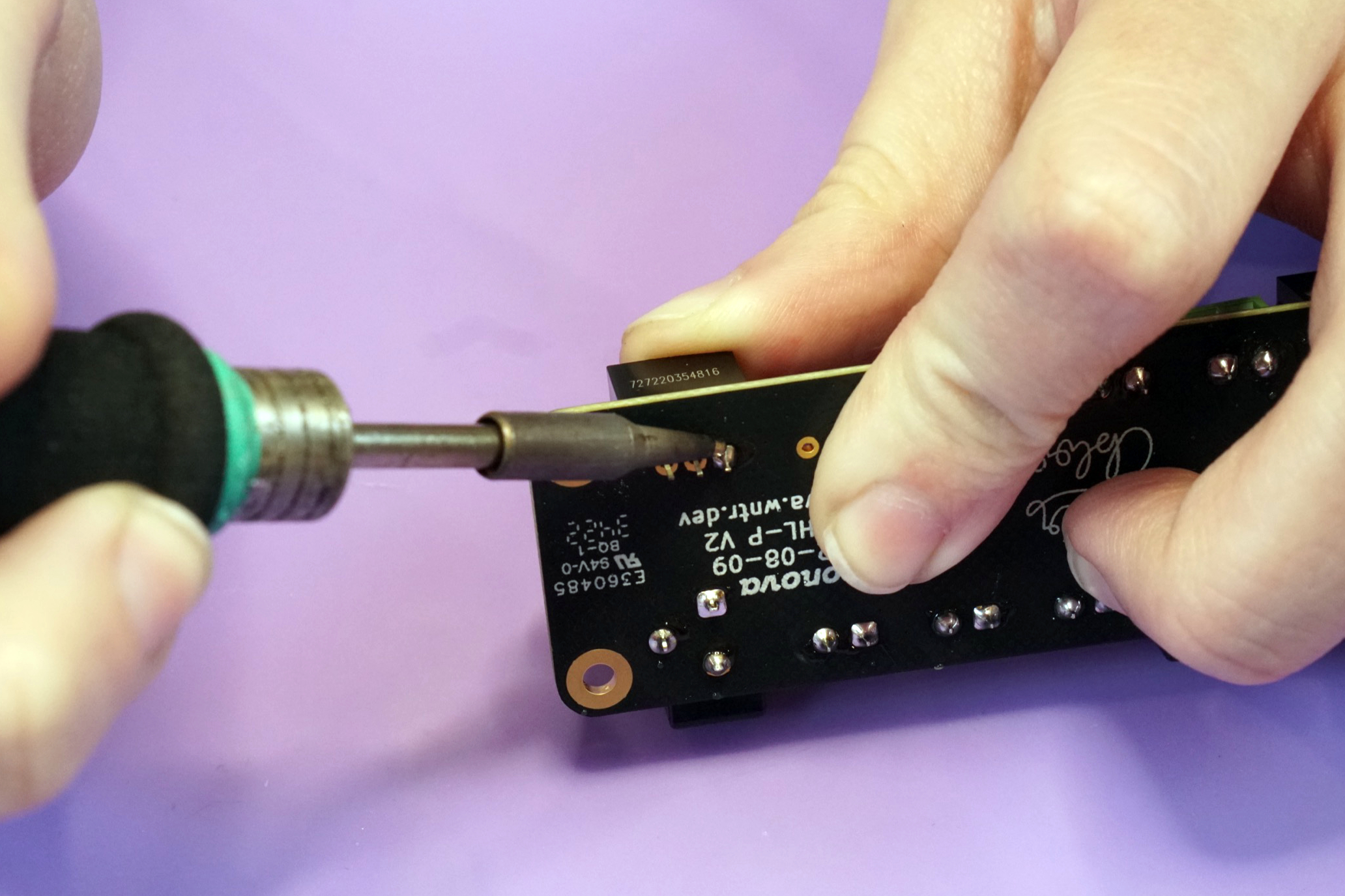 Photo of the 5V converter being pushed flush against the board while heat is applied to the solder joint using a soldering iron